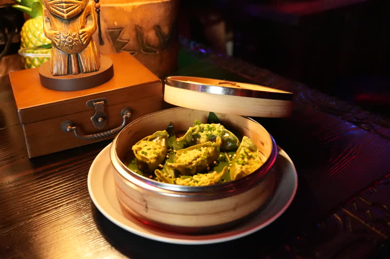 Handmade dumplings in bamboo steamer alongside tiki statue at Kaona Room